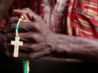 man holding rosary in hands - godongphoto/Shutterstock.com