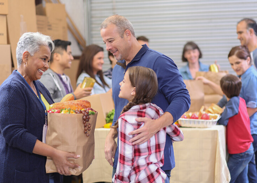 community service day - woman holding brown bag talks to man with his daughter - fstop123/E+/Getty Images