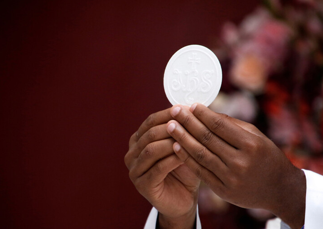 close-up of priest's hands as he holds Communion host - Sidney de Almeida/Shutterstock.com