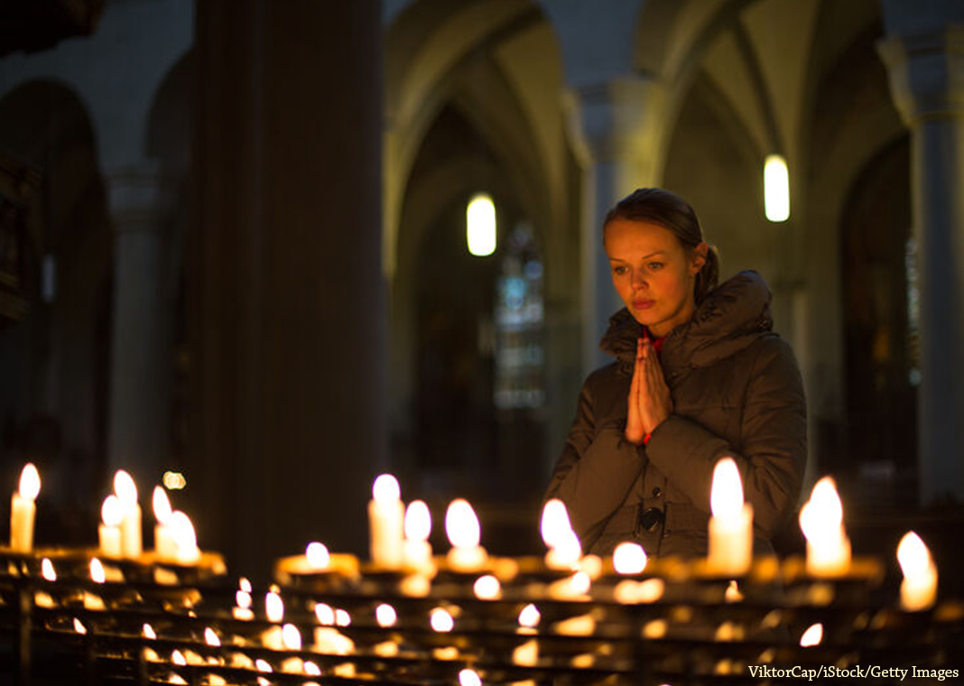 woman praying in church near candles - ViktorCap/iStock/Getty Images